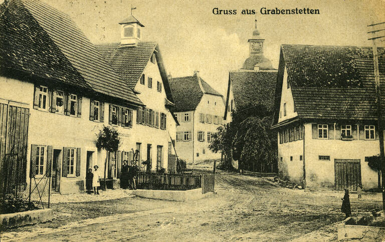 Historische unbunte Fotografie einer Straße in Grabenstetten. Es handelt sich um eine Ansichtskarte mit der Aufschrift "Gruss aus Grabenstetten".
