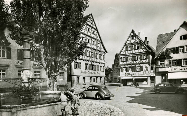 Historische Schwarzweißfotografie des Marktplatzes von Münsingen. Zu sehen ist unter anderem der Marktbrunnen.